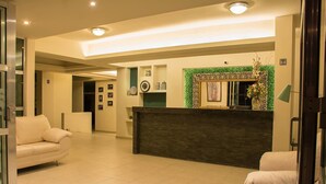 A hotel lobby with a reception desk, a sofa, and a decorative wall. - Hotel Siena (Penjamo)