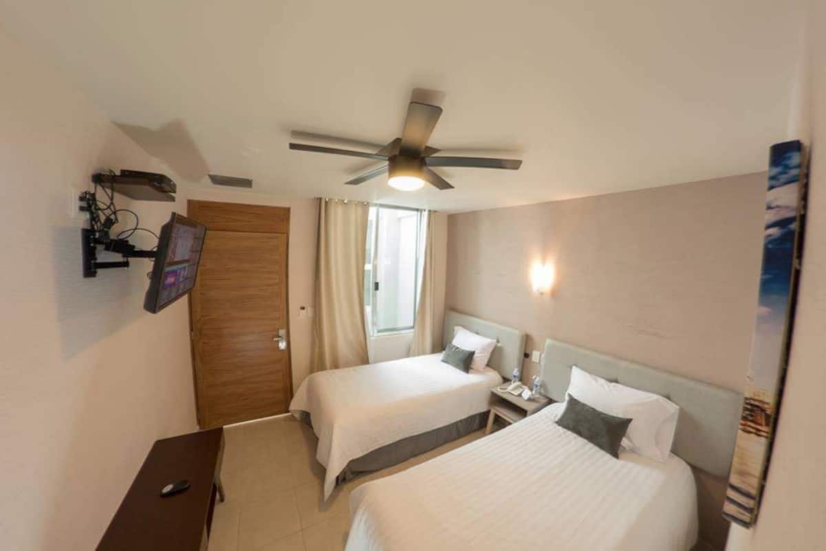 A hotel room with two beds, a ceiling fan, a TV mounted on the wall, and a window with curtains.