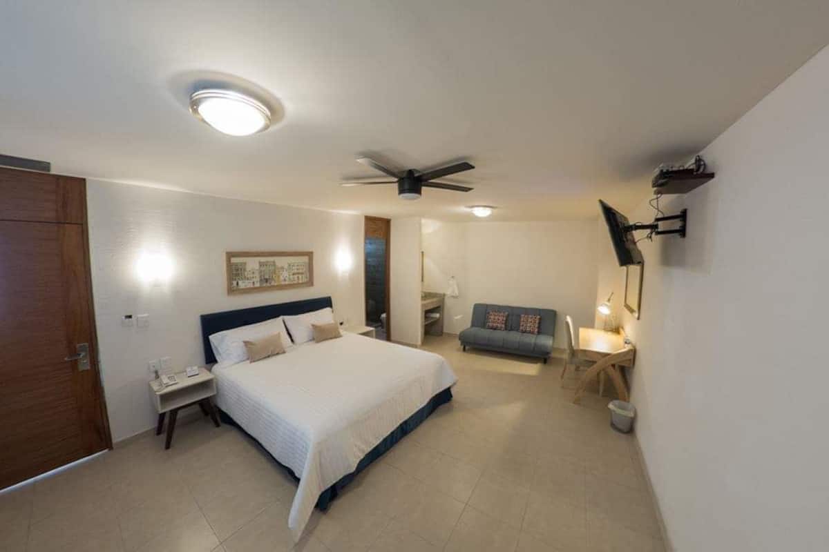 A bedroom with a bed, a ceiling fan, a TV mounted on the wall, and a small desk with a chair.