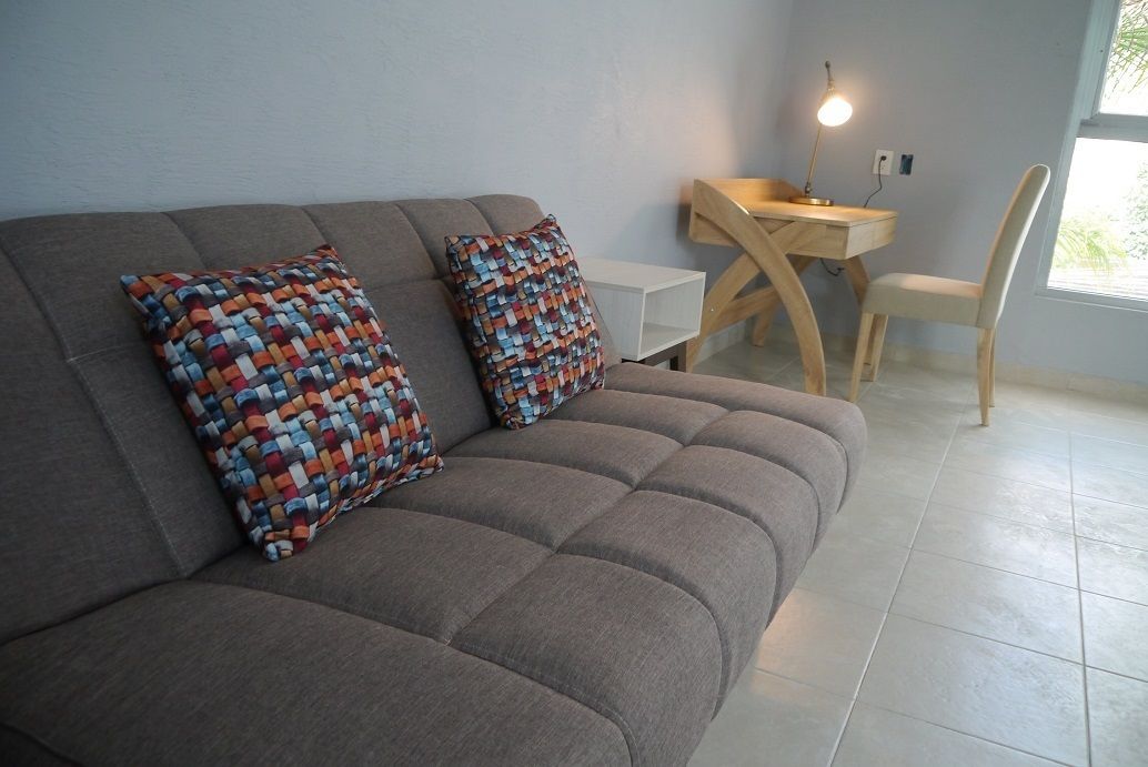 Un soggiorno moderno con un divano grigio, due cuscini colorati, una piccola scrivania in legno con una lampada e una sedia bianca.