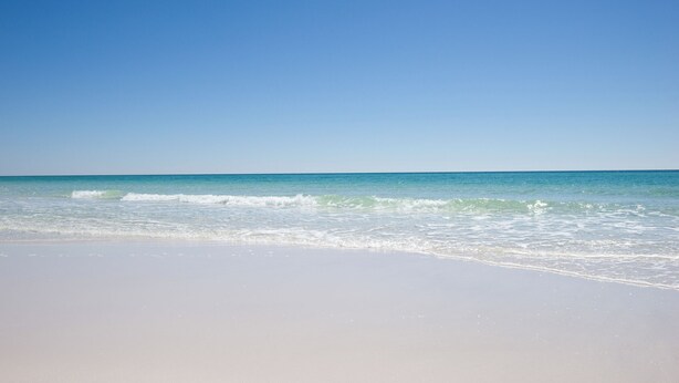 Una platja amb cel blau i ones tranquil·les.
