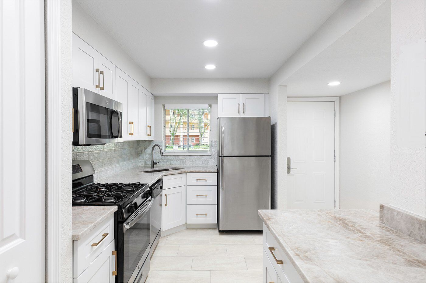 A modern kitchen with white cabinetry, stainless steel appliances, and a marble countertop.