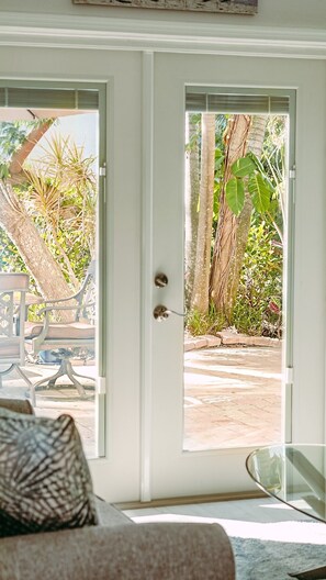 Ein Zimmer mit Blick durch eine Glastür auf einen Außenbereich mit Terrasse, Stühlen und Grünpflanzen.