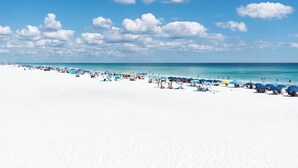 Ein Strand mit weißem Sand, klarem blauen Wasser und vereinzelten Sonnenschirmen.