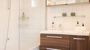 Un bagno moderno con doccia vetrata, una vasca da bagno bianca e un mobile vanitario con pensili in legno e piano di lavoro bianco.