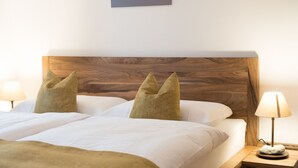 Un letto matrimoniale con testiera in legno, due cuscini e un comodino con una lampada.