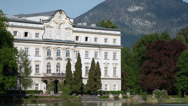 Ein großes, klassizistisches Gebäude mit symmetrischer Architektur, einem markanten Haupteingang und einem umlaufenden Garten mit einem Wasserbecken.