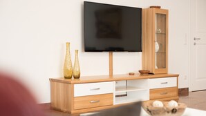 A modern living room with a wooden TV stand, a flat-screen TV, and a glass-fronted cabinet.
