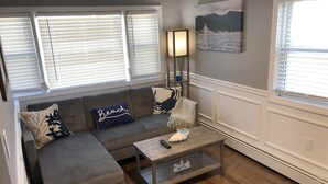 A living room with a gray sectional sofa, a coffee table, and a painting of a lighthouse. - "THE PLACE AT SUNRISE BEACH" (Marshfield)