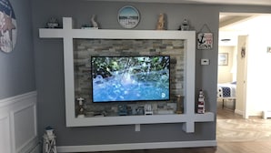 A living room with a mounted TV, stone fireplace, and decorative items on shelves. - "THE PLACE AT SUNRISE BEACH" (Marshfield)