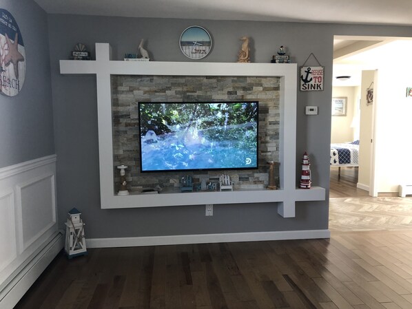 A living room with a mounted TV, stone fireplace, and decorative items on shelves.