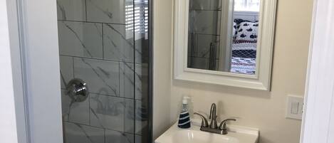 Ein Badezimmer mit einer Duschkabine aus Glas, einem weißen Waschbecken mit Spiegel darüber und einem kleinen Schrank darunter.