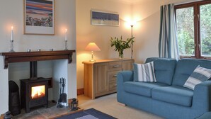 A cozy living room with a fireplace, a sofa, a lamp, and a window with curtains. - 2 bedroom accommodation in Arduaine, near Oban (Arduaine, near Oban)