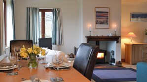 A dining room with a wooden table set for a meal, a fireplace, and a painting on the wall. - 2 bedroom accommodation in Arduaine, near Oban (Arduaine, near Oban)