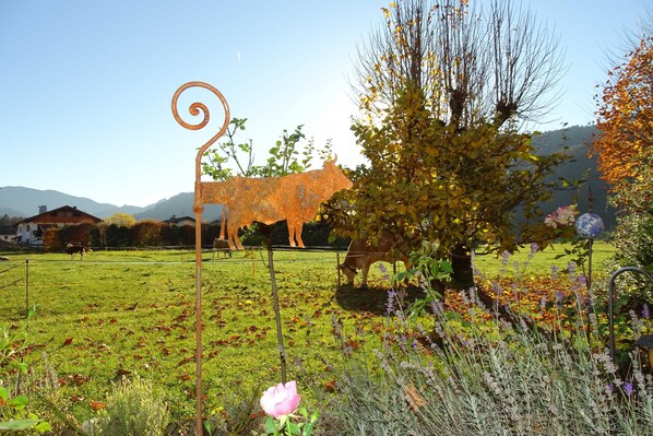 A rural landscape with a metal sculpture of a cow, a tree, and a field.