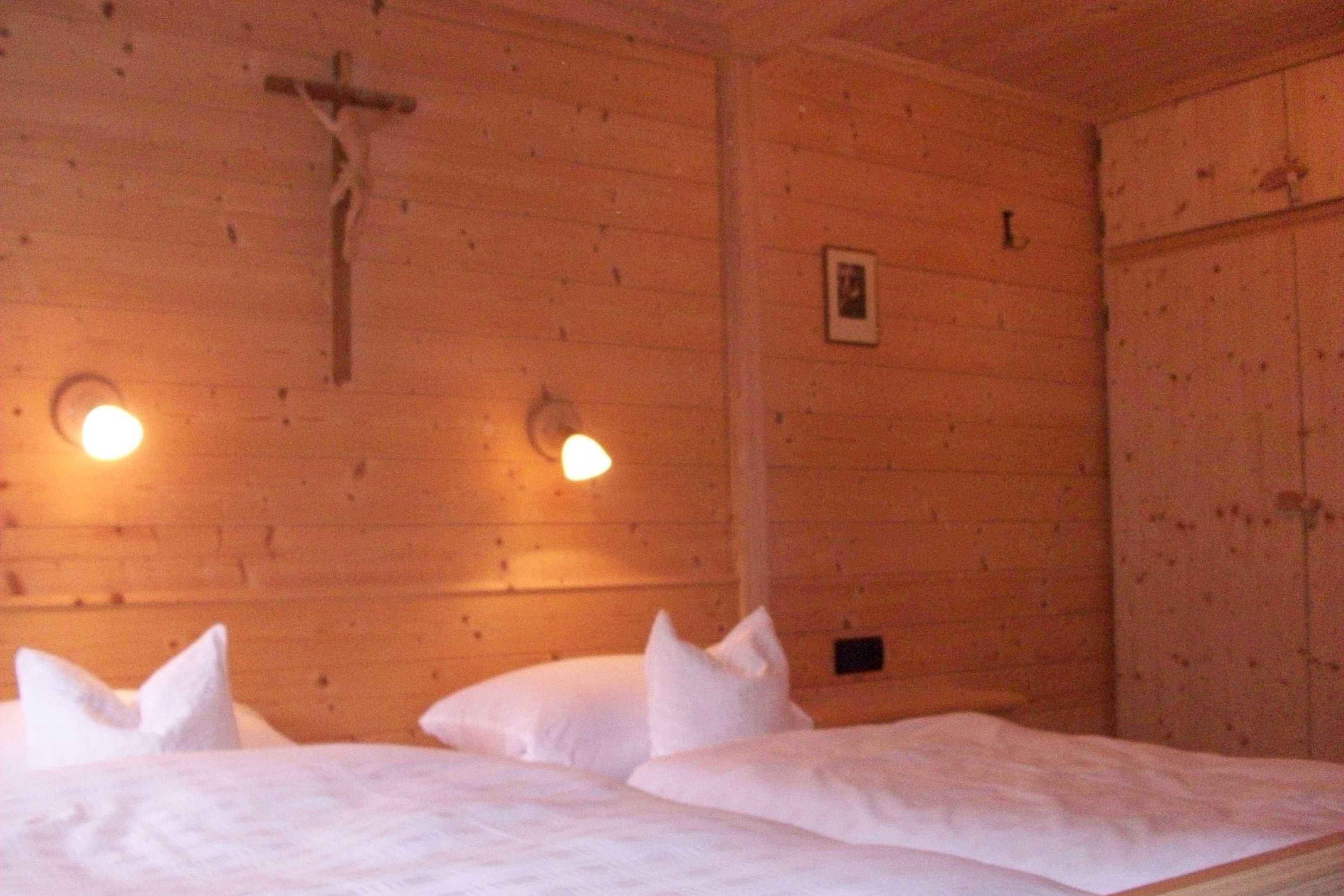 A wooden room with a cross on the wall, two beds with white bedding, and wall-mounted lights.