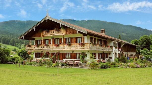 Een chalet met twee verdiepingen, met balkons, een houten gevel en een berg op de achtergrond.