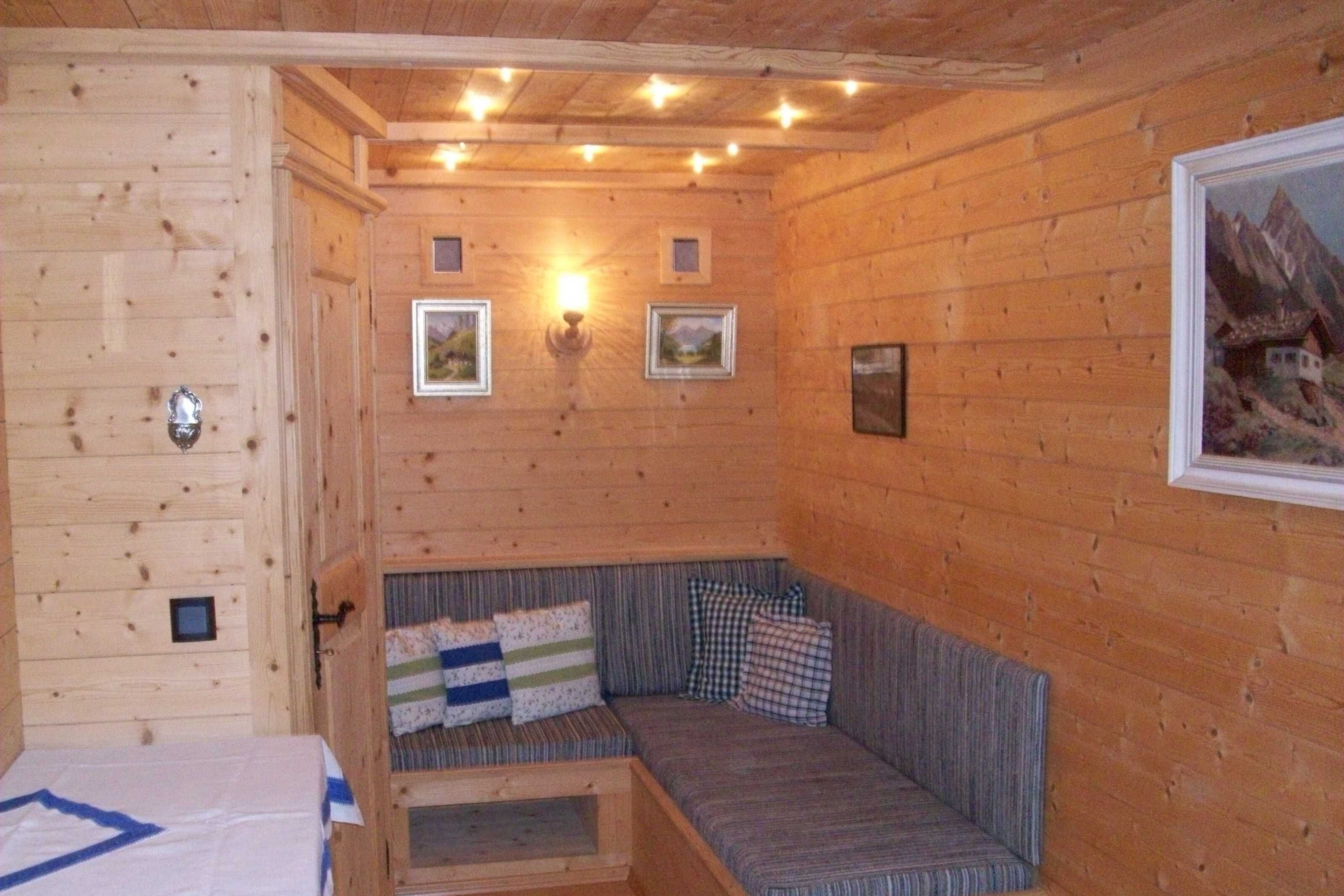 Een houten blokhut van binnen, met een bank, foto's in lijsten aan de wanden en een bed.