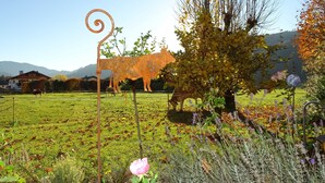 Een landelijk landschap met een metalen sculptuur van een koe, een boom en een veld.