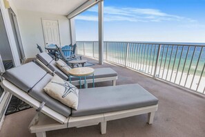 A balcony with two sunbeds, a small table, and a chair. - Regency Isle 1008 | Beachfront Condo w/ Pools & Gulf Views, Near (Orange Beach)