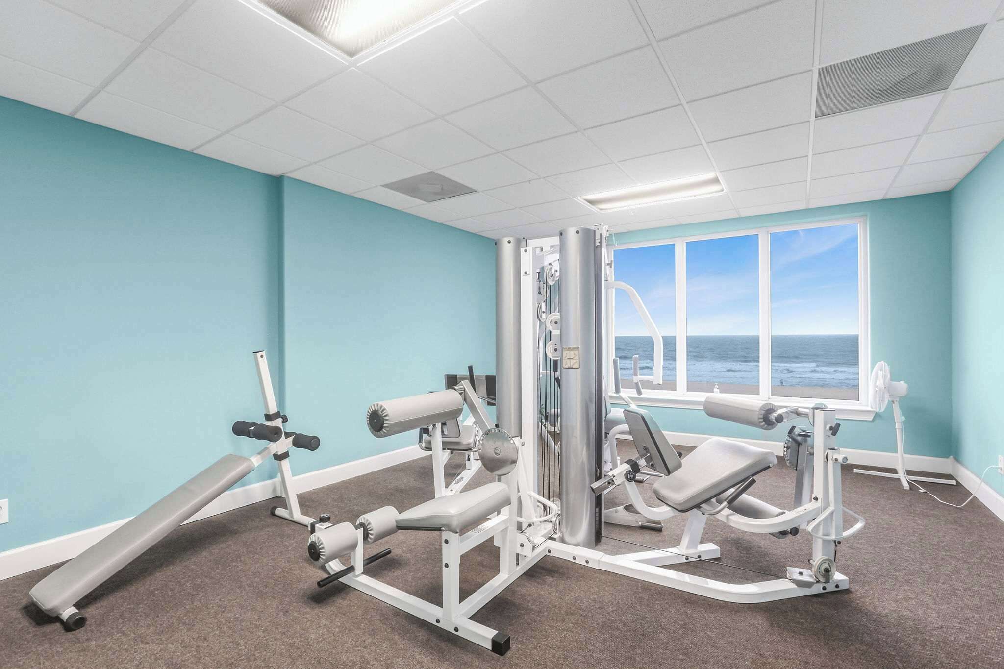 A gym with exercise equipment, a bench, and a window with a view of the ocean.