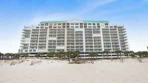 Een hotel met meerdere verdiepingen en een plat dak, gelegen aan een zandstrand met palmbomen.