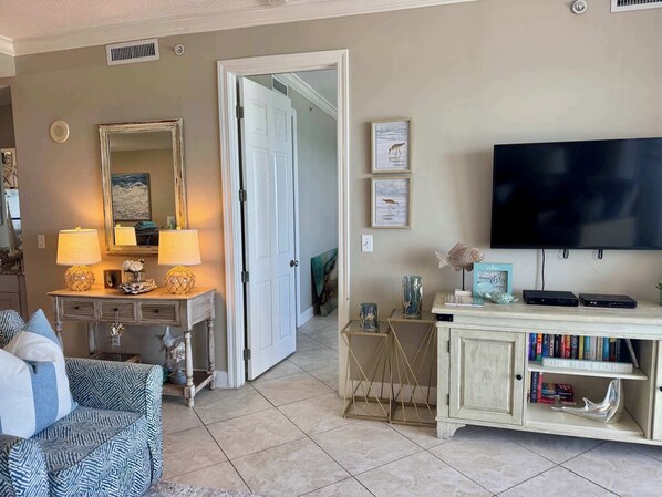 A living room with a television, a coffee table with decorative items, a sofa, and a bookshelf with books and a welcome sign.