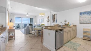 Een moderne keuken met een centraal eiland, een eethoek met stoelen en uitzicht op een balkon.