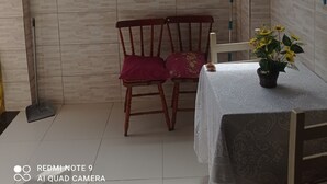 A room with a tiled floor, a wooden chair with a red cushion, a small table with a white tablecloth, and a potted plant with yellow flowers. - Family home (Sítio do Campo)