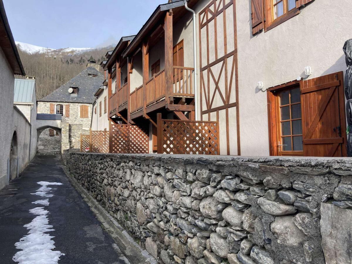 A narrow street with stone walls and wooden buildings, featuring balconies and a stone archway.