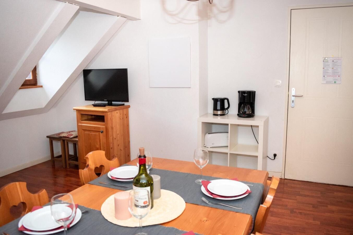 Un coin repas avec une table dressée pour deux personnes, un téléviseur, une machine à café et un tableau blanc fixé au mur.