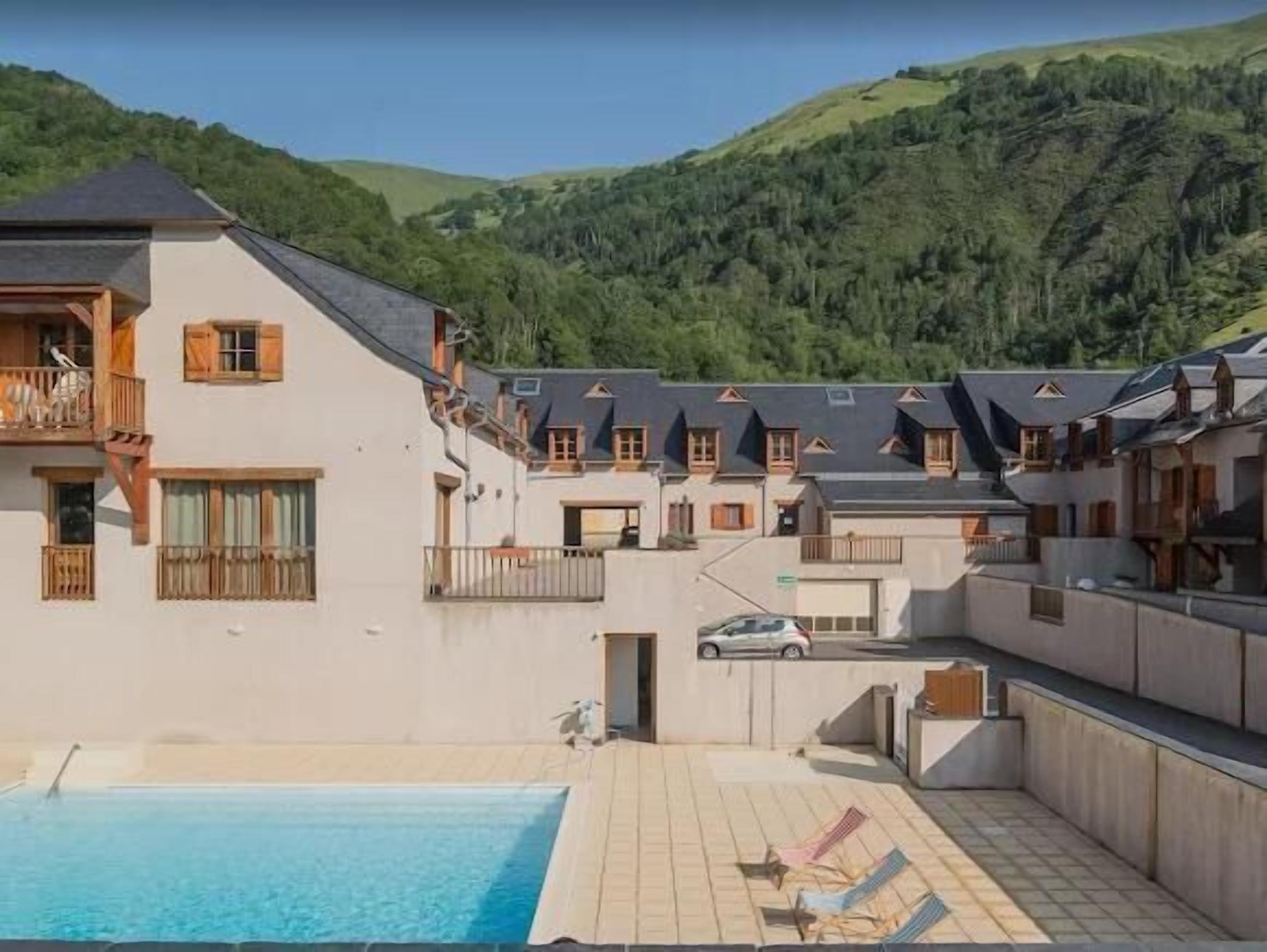 A hotel with a swimming pool, multiple balconies, and a view of the surrounding hills.