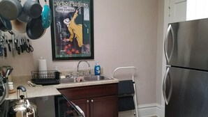 Une cuisine équipée d’une cuisinière, d’un évier et d’un réfrigérateur. Une affiche est accrochée au mur et divers ustensiles de cuisine sont suspendus au-dessus de l’évier.