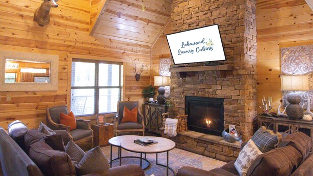 A cozy cabin interior with a stone fireplace, wooden walls, and a ceiling fan.