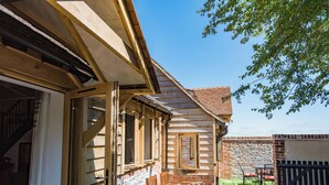 A wooden house with a brick exterior, a patio with a table and chairs, and a stone wall in the background.