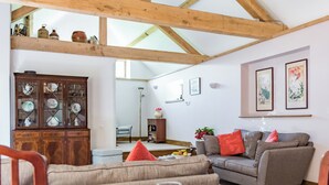 A cozy living room with a dining area, wooden beams on the ceiling, a cabinet with glass doors, and a sofa with cushions.
