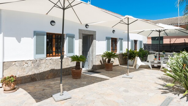 A courtyard with white buildings, potted plants, outdoor furniture, and umbrellas. - CAN BLAU - Cosy chalet with garden and terraces near the beach. Free WiFi (Alcúdia)