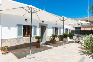 Une cour intérieure avec des bâtiments blancs, des plantes en pot, du mobilier d’extérieur et des parasols.