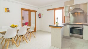 A modern kitchen with a built-in oven, a dining area with white chairs and a table, and a small island with a plant. - CAN BLAU - Cosy chalet with garden and terraces near the beach. Free WiFi (Alcúdia)