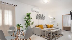 A modern living room with a sofa, coffee table, and chairs. There is a potted plant and a wall-mounted air conditioner. - CAN BLAU - Cosy chalet with garden and terraces near the beach. Free WiFi (Alcúdia)