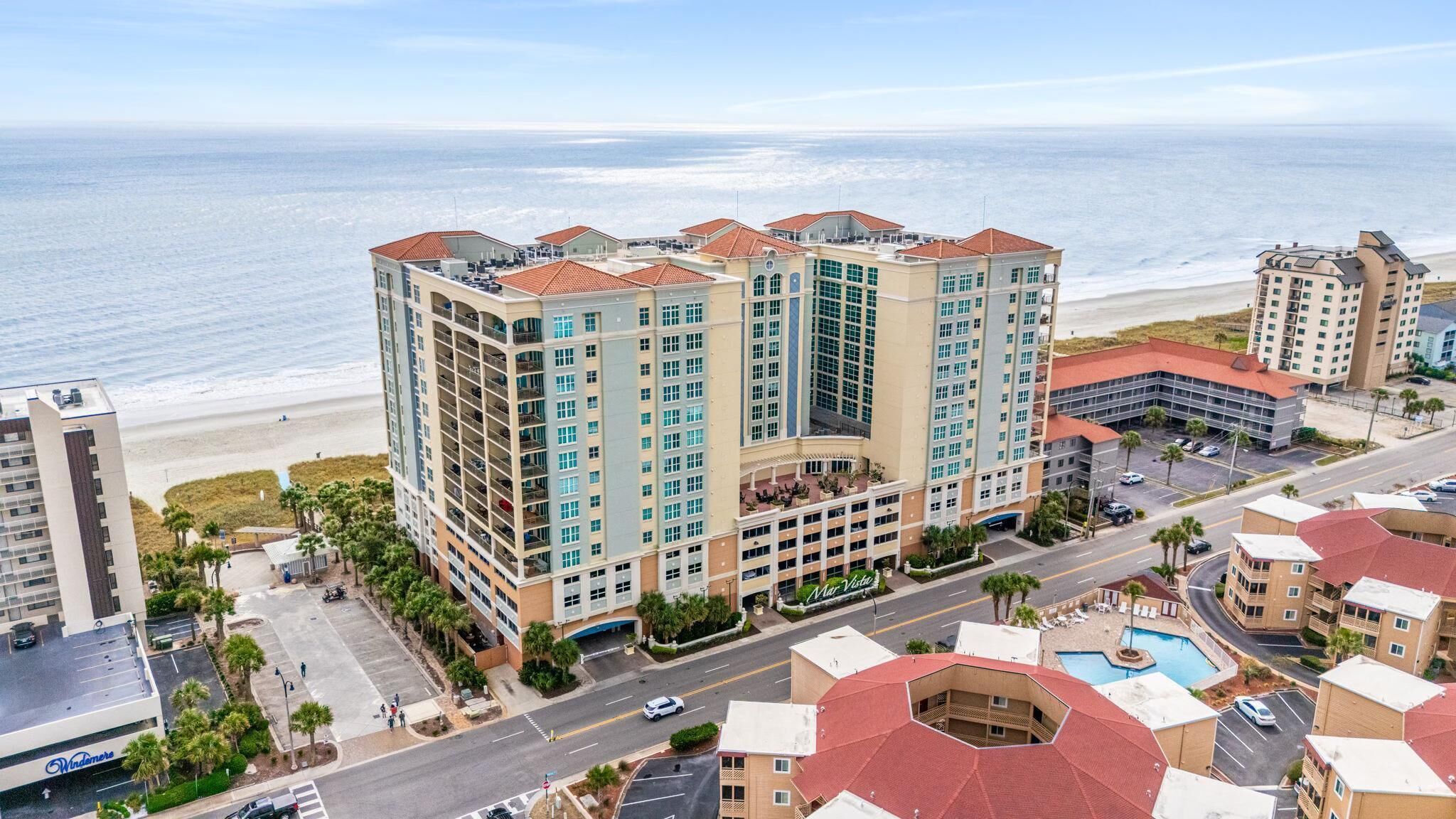 A multi-story hotel with a central courtyard, a pool, and a view of the beach.