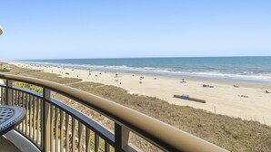 A beach view from a balcony with a railing, beach chairs, and umbrellas.