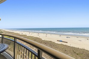 Blick auf den Strand von einem Balkon mit Geländer, Liegestühlen und Sonnenschirmen.