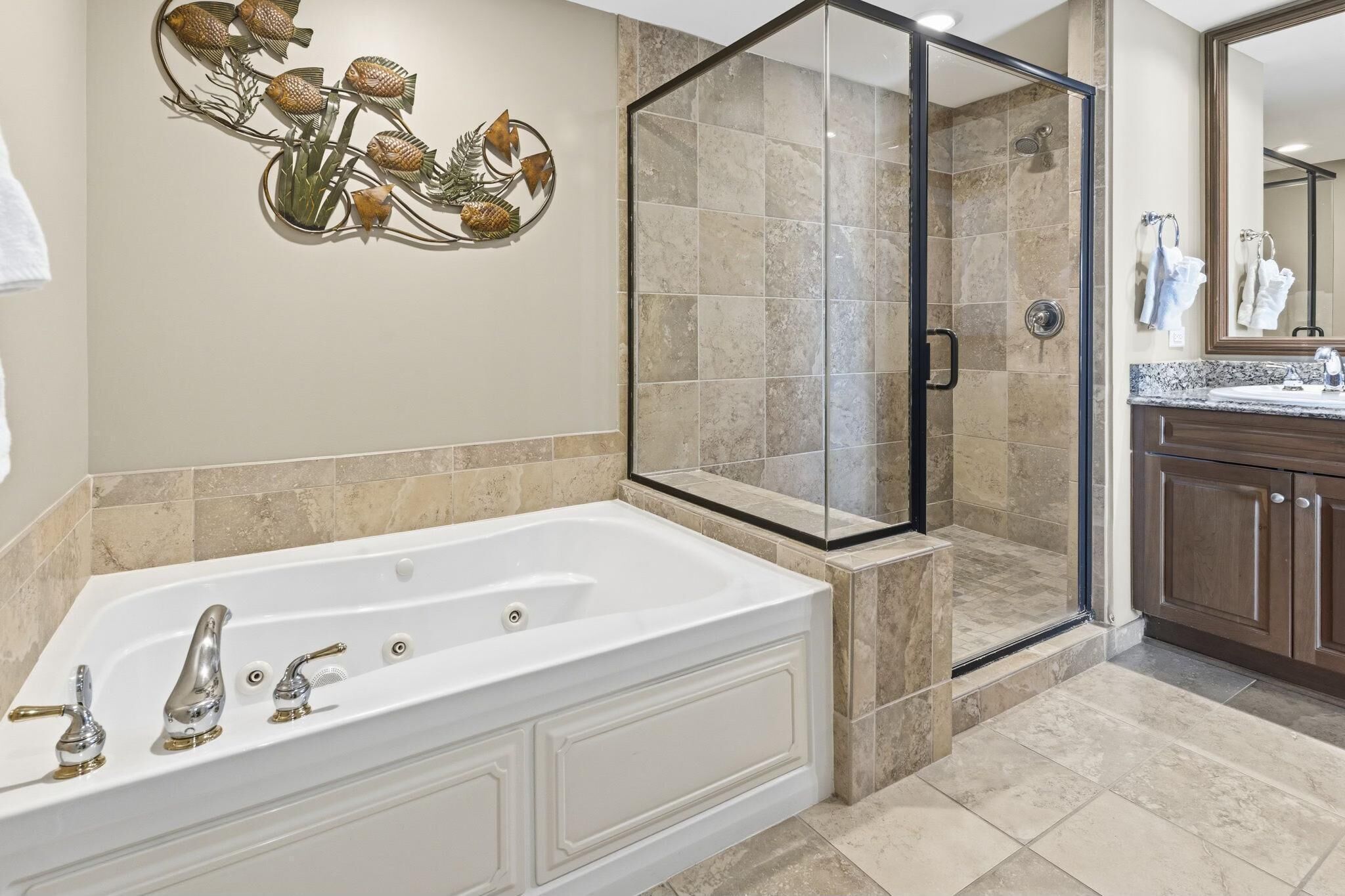 A bathroom with a large white bathtub, a glass-enclosed shower, and a wall-mounted fish decoration.