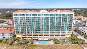 A multi-story hotel with numerous balconies, a swimming pool, and a parking area.