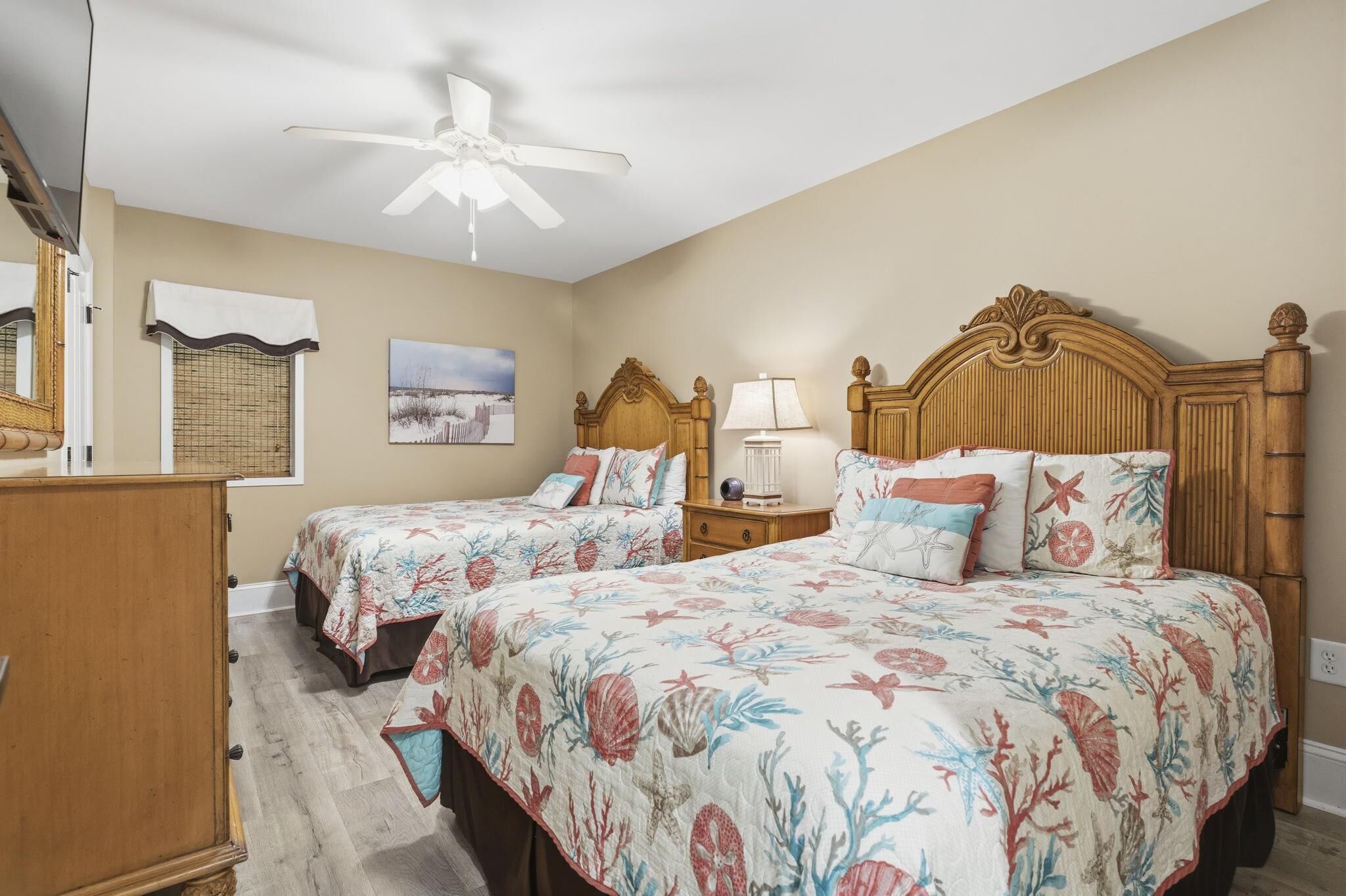 A bedroom with two beds, a ceiling fan, a nightstand, a lamp, and a window with a view.