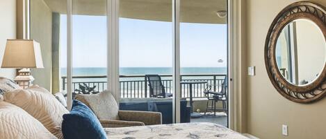 A hotel room with a bed, a large window, a balcony, and a round mirror on the wall.