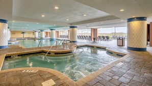 An indoor swimming pool with a 3 FT depth marker, lounge chairs, and a view of the outside.