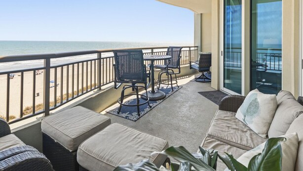 A balcony with a view of the beach, outdoor furniture, and a sliding glass door.