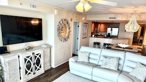 A modern living room with a large flat-screen TV, a white leather sofa, and a dining area with a chandelier. - MVG 509 Oceanfront Club floor (North Myrtle Beach)